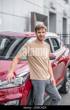 Smiling young male leaning on red car outside Stock Photo
