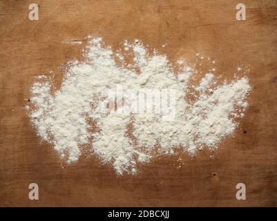 white wheat flour scattered on a brown wooden table, top view, kitchen backdrop Stock Photo