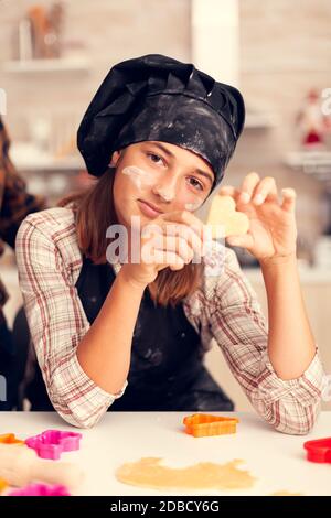 Childs hands with heart shaped pastry on christmas day wearing apron and bonette. Happy cheerful joyfull teenage girl helping senior woman preparing sweet cookies to celebrate winter holidays. Stock Photo