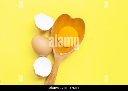 Egg yolk and white on  wooden spoon heart shape on yellow background.  . Top view Stock Photo