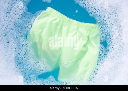 Green baby shorts soak in baby laundry detergent water dissolution, washing cloth, blue background, Laundry concept. Stock Photo