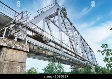 Iron train bridge over the river against a cloudy sky. Bridge in greenery Stock Photo