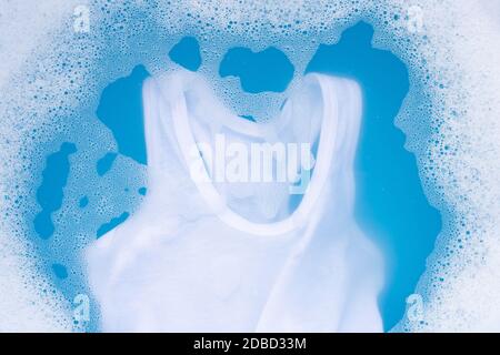 White kid undershirt soak in baby laundry detergent water dissolution, washing cloth, blue background, Laundry concept. Stock Photo