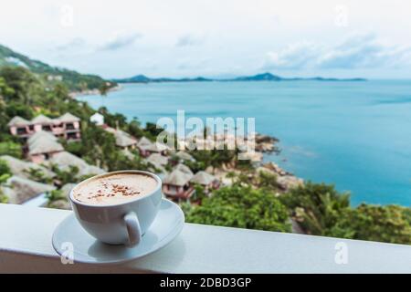 A cup of coffee stands on the window with a beautiful view of the ocean on the tropical island Stock Photo