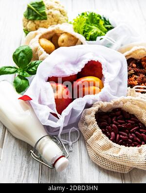 Fresh fruits and vegetables in eco cotton bags on table in the kitchen. Milk,  potatoes, apricots, rucola, beans from market. zero waste shopping conc Stock Photo