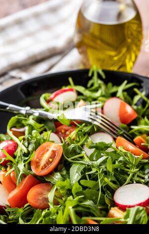 Fresh arugula salad with radishes, tomatoes and red peppers on plate. Stock Photo