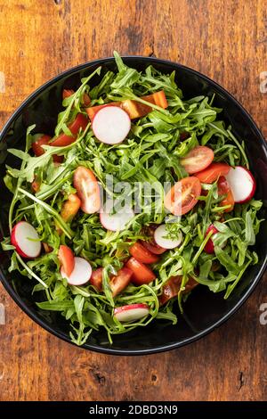 Fresh arugula salad with radishes, tomatoes and red peppers on plate. Top view. Stock Photo