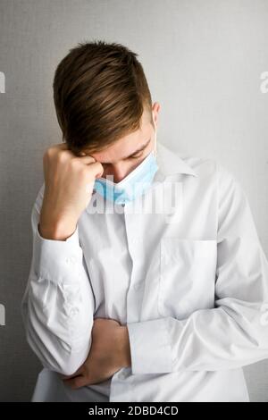 Sad and Tired Young Man in a Flu Mask by the Wall in the Room Stock Photo