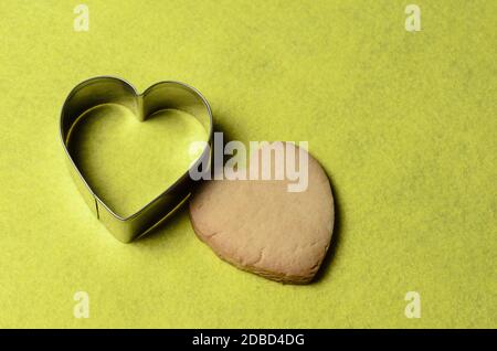 Homemade cookies with a metal baking dish in the shape of a heart on a yellow background. Selective focus. Stock Photo