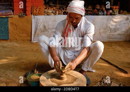 Indian potter at work: throwing the potter's wheel and shaping ceramic vessel and clay ware: pot, jar in pottery workshop. Experienced master. Handwor Stock Photo