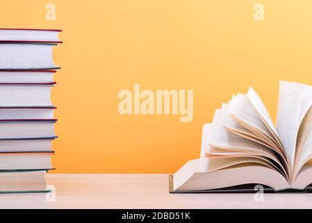 A large, thick hardcover book is lying on a light wood table. The book is open, next to a stack of closed books, and on the back is a yellow backgroun Stock Photo