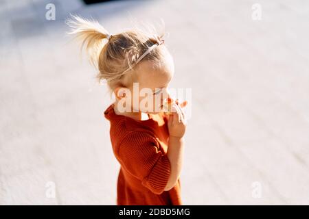 A pretty little girl with a pink bow in her hair is eating a pie on a sunny day Stock Photo