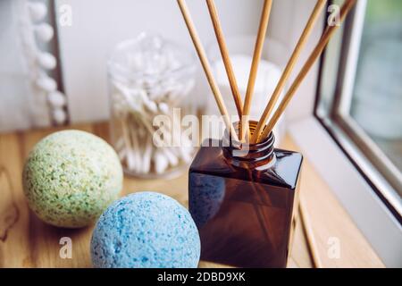 Natural wooden bathroom window sill with liquid diffuser bottle with wood sticks, natural light coming from window. Blue and green soothing bath bombs. Stock Photo