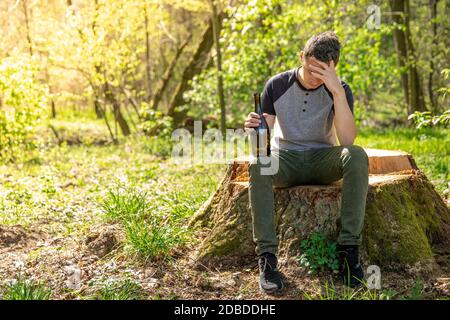 alcohol as a solution to a problem, a worried man with a bottle in his hand thinking about worries in the woods Stock Photo