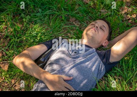 drunk man with a bottle of alcohol under his arm resting on a green field. Stock Photo