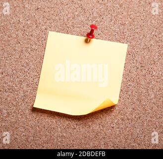 Blank yellow sticky note pinned on a cork bulletin board. Stock photo Stock Photo