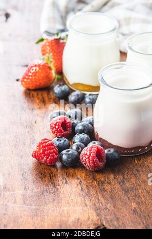 White fruity yogurt in jar and blueberries, raspberries, strawberries on wooden table. Stock Photo