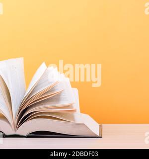 A large, thick hardcover book is lying on a light wood table. The book is open, next to a stack of closed books, and on the back is a yellow backgroun Stock Photo