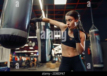 Woman in black boxing bandages and sportswear hits a punching bag, box training. Female boxer in gym, girl kickboxer in sport club, punches practice Stock Photo