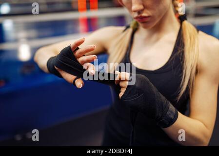 Woman winds up black bandages before boxing training. Female boxer in gym, girl kickboxer in sport club, punches practice, arms care Stock Photo