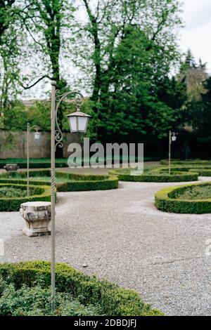 Gray street lamps in the grass on the park alley with manicured lawns. Stock Photo