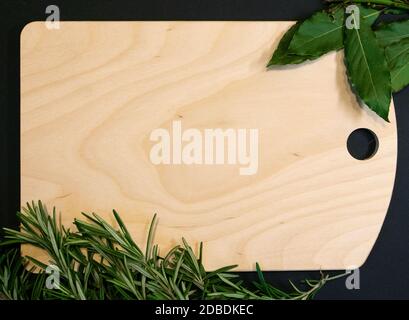 Cutting board of light wood framed with bay leaves and rosemary sprigs, designer template Stock Photo