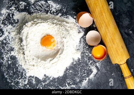 Ingredients for baking - dough, flour, rolling pin, eggs, egg yolks on a dark background. Top views, close-up. Stock Photo