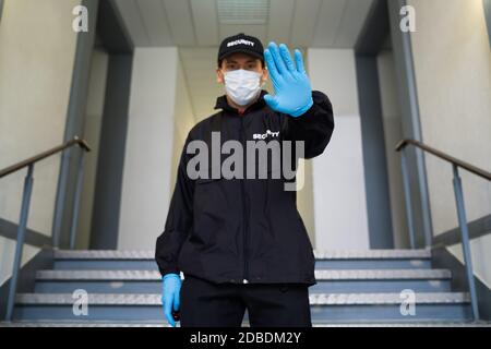 Security Guard In Face Mask Making Stop Gesture At Entrance Stock Photo