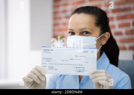 Woman In Face Mask Holding Paycheck Or Stimulus Check Stock Photo