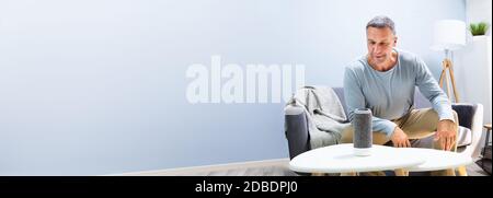 Senior Man Using Smart Home Speaker And Voice Assistant Stock Photo