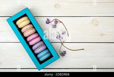 Macaroons in gift box next to violet on wooden background Stock Photo