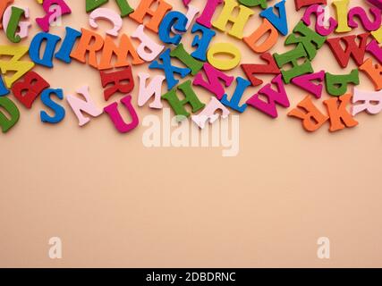 multi-colored wooden letters of the English alphabet on a beige background, top view, copy space Stock Photo