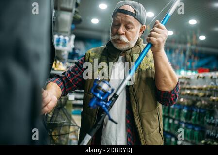 Male angler choosing rod in fishing shop. Equipment and tools for fish catching and hunting, accessory choice on showcase in store, spinnings and tele Stock Photo