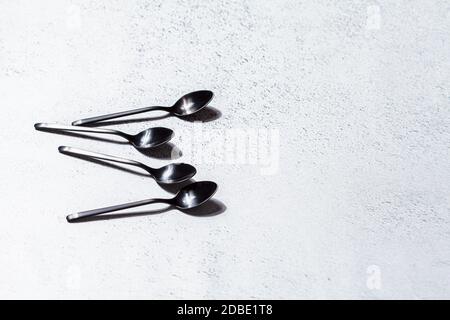 Empty black dessert spoons on gray background, copy space. Eating food concept. Stock Photo