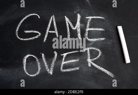 inscription in English game over with white chalk on a black board, concept of ending the process Stock Photo