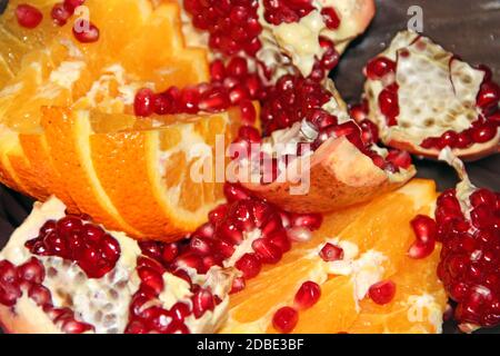 Sliced orange slices and broken ripe pomegranate close up. Orange segments and ripe seeds of pomegranate. delicious fruits. Useful food. Health care. Stock Photo