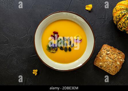 Flat lay of pumpkin cream soup with edible flowers, seeds, and fresh baked bread. Healthy vegan autumn lunch. Stock Photo