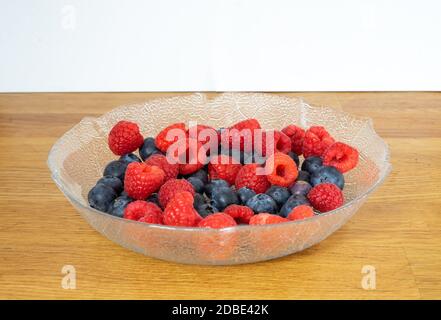 mixed berries strawberries blueberries and raspberries served in a glass bowl. standing in the kitchen against a wood background white Stock Photo