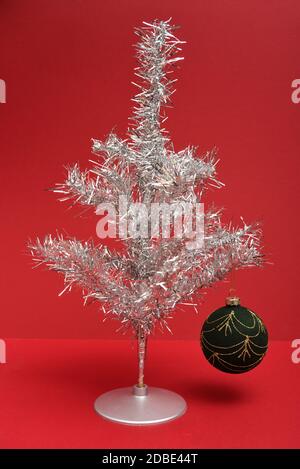 Retro silver tinsel Christmas tree with bauble on a red background Stock Photo