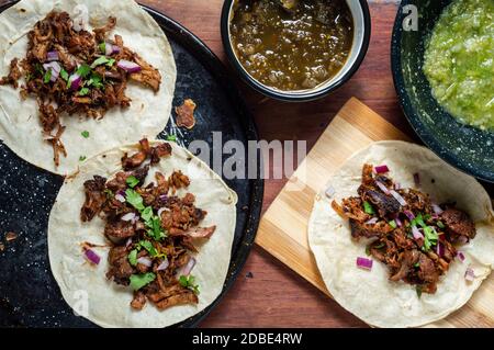 Carnitas tacos with red onion and raw salsa verde. Mexican slow cooked pork dish from Michoacan with fresh green salsa Stock Photo