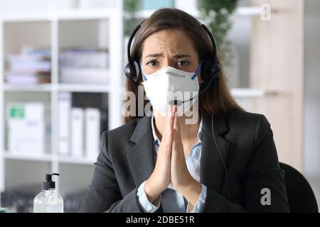 Sad telemarketer woman begging looking camera avoiding covid-19 with mask sitting at the office at night Stock Photo