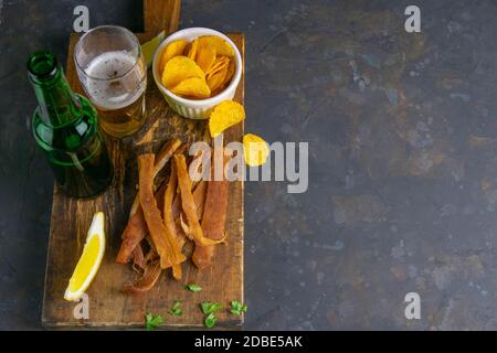 Peruvian squid with beer, lemon and potato chips on dark wooden board. Snack on fish with beer. Top views with clear space. Stock Photo