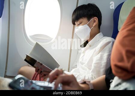 fifteen year old boy on airplane wearing face mask reading a book Stock Photo