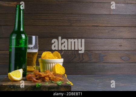 Peruvian squid with beer, lemon and potato chips on dark wooden board. Snack on fish with beer. Front views with clear space. Stock Photo