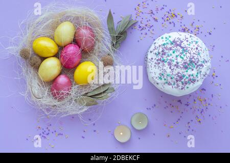 Easter eggs in the nest, cake, candles on a purple background Stock Photo