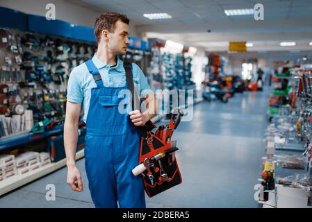 Male worker in uniform holds toolbox in tool store. Choice of professional equipment in hardware shop Stock Photo