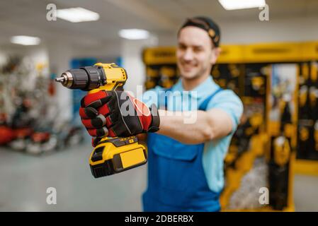 Male worker holds battery powered screwdriver in tool store. Choice of professional equipment in hardware shop, electrical instrument supermarket Stock Photo