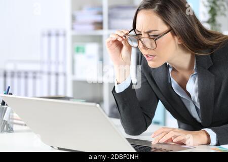 Executive woman with eyeglasses having eyesight problems trying to read on laptop sitting on her desk at office Stock Photo
