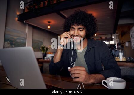 Handsome young man with curly hair watching videos on laptop with earphones in cafe Stock Photo