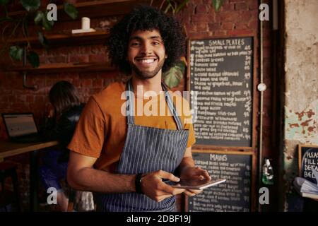 Successful small cafe business owner wearing apron using digital tablet and looking at camera Stock Photo